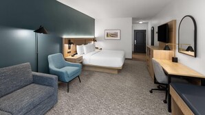 Una habitación de hotel moderna con cama, escritorio, silla, sofá y un espejo grande.