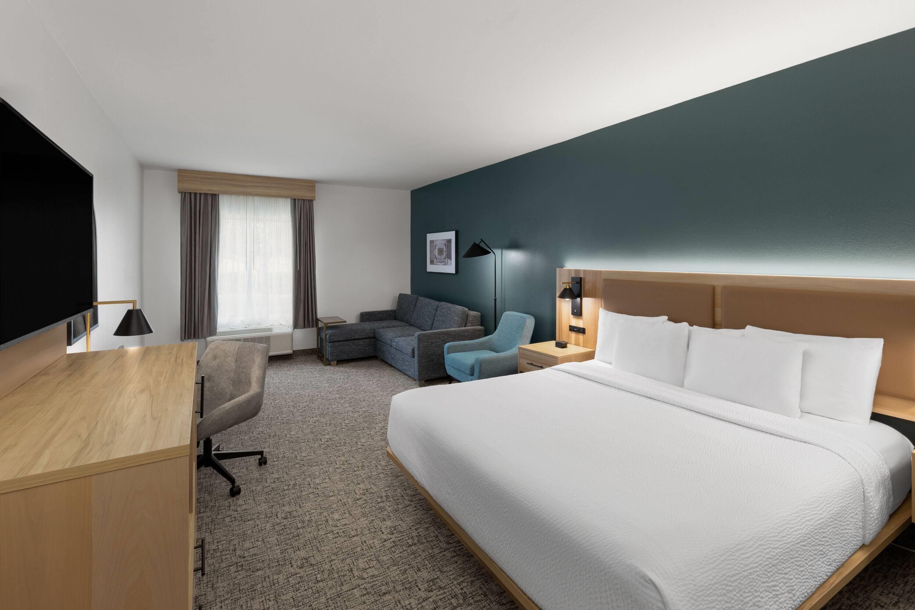 Habitación de hotel con una cama grande, un escritorio, una silla, un sofá y una mesita de noche.