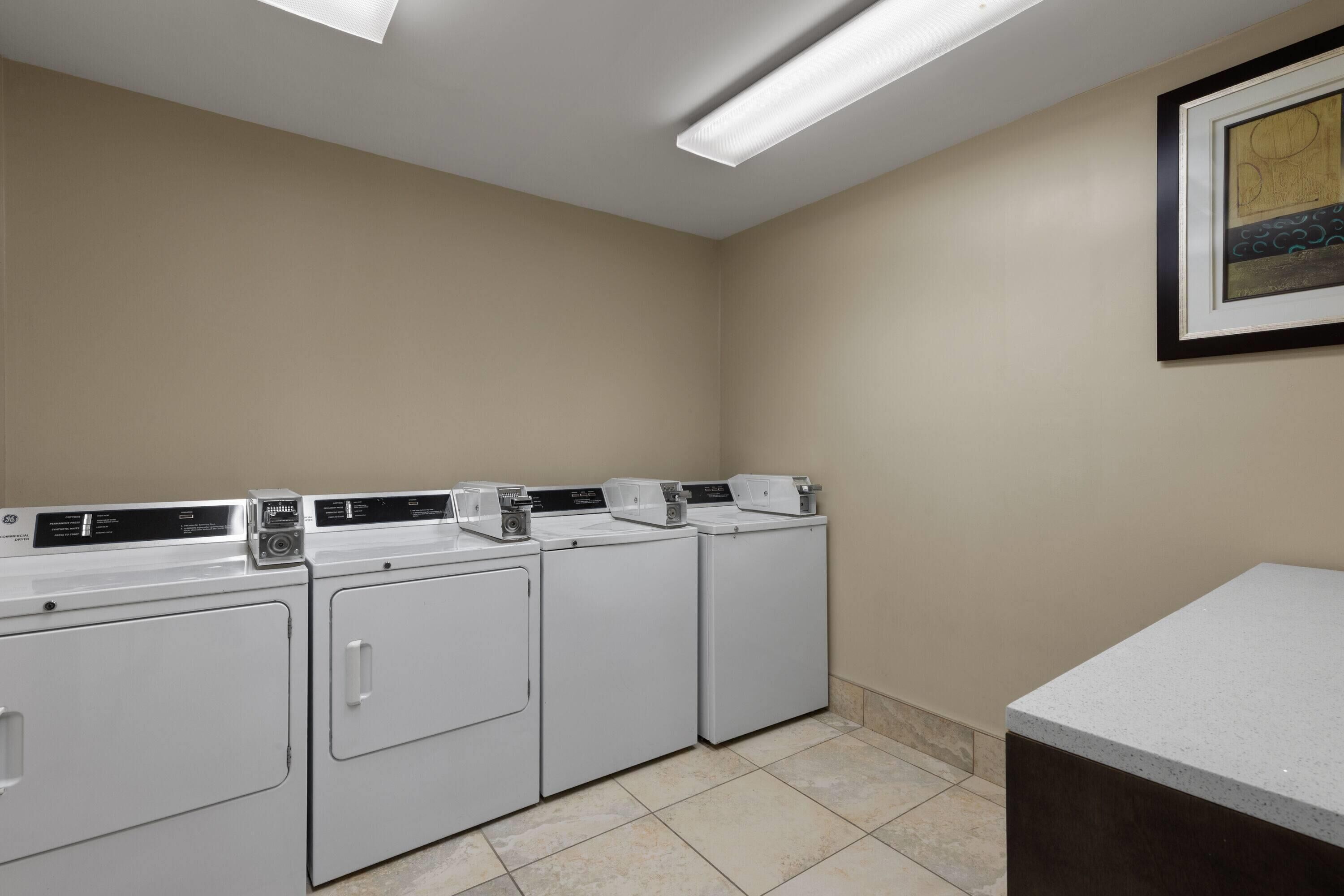 A laundry room with four white front-loading washing machines, a countertop, and a framed artwork on the wall.
