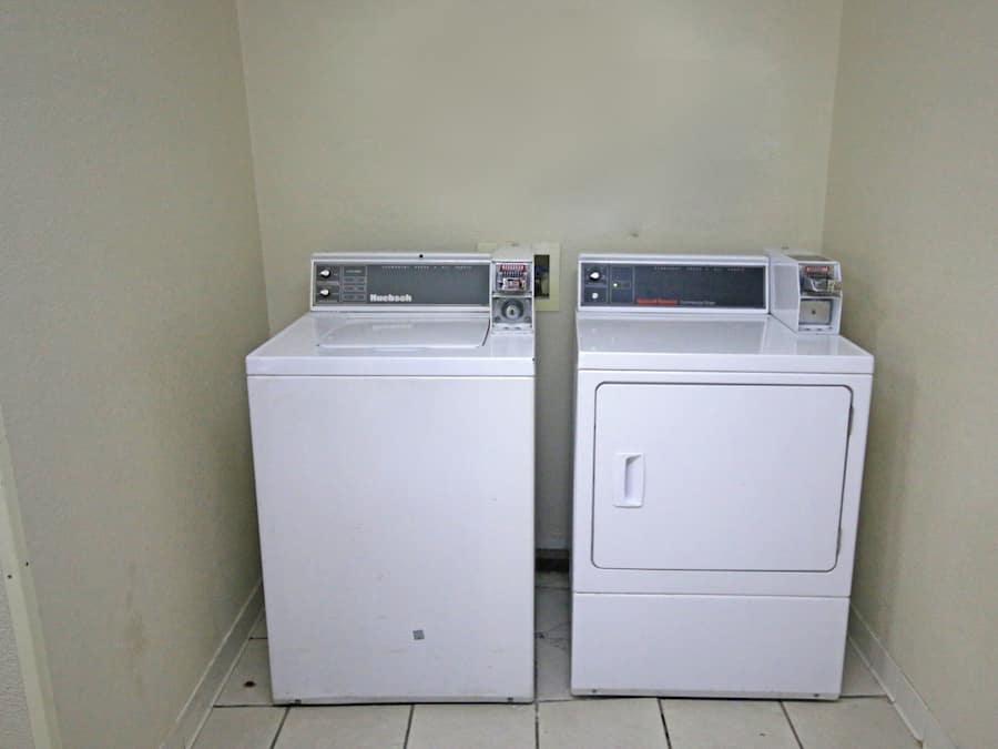 Two white front-loading washing machines in a corner with a tiled floor.