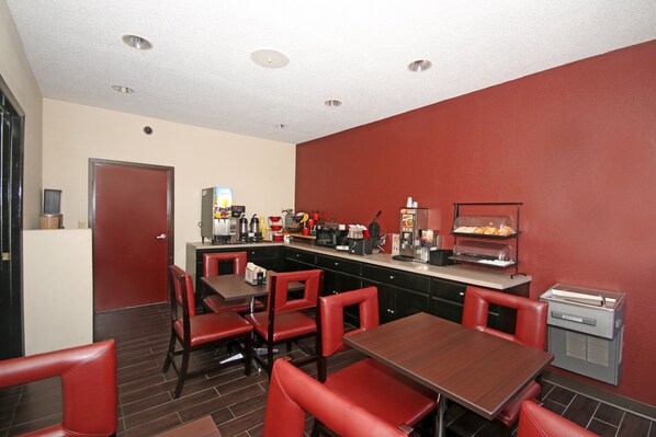 A restaurant with red chairs, a counter with a coffee machine, and a refrigerator.