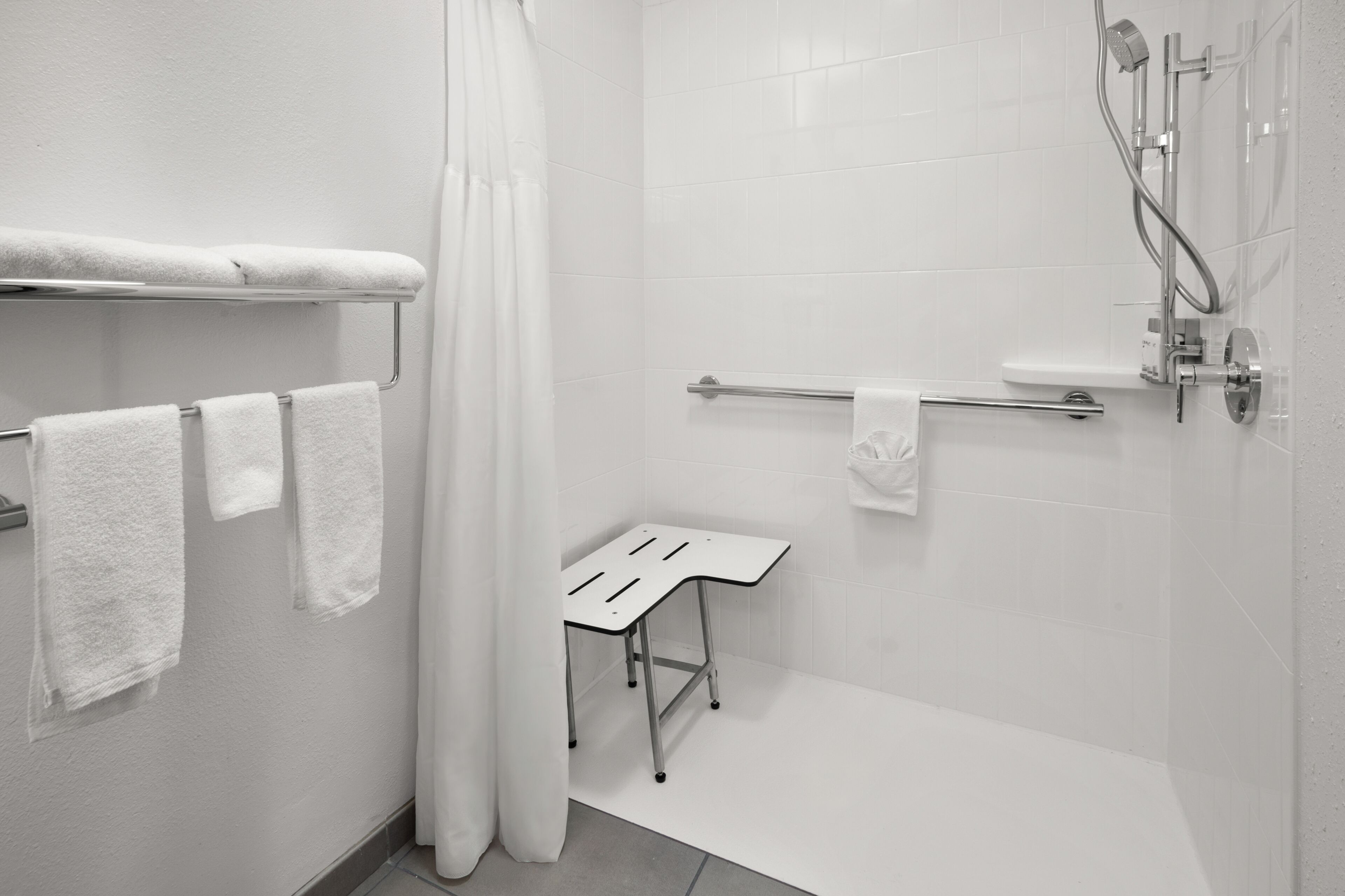 A modern bathroom with white tiles, a shower, a towel rack, and a small table.