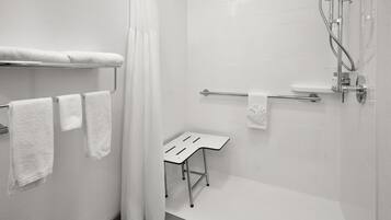 A modern bathroom with white tiles, a shower, a towel rack, and a small table.