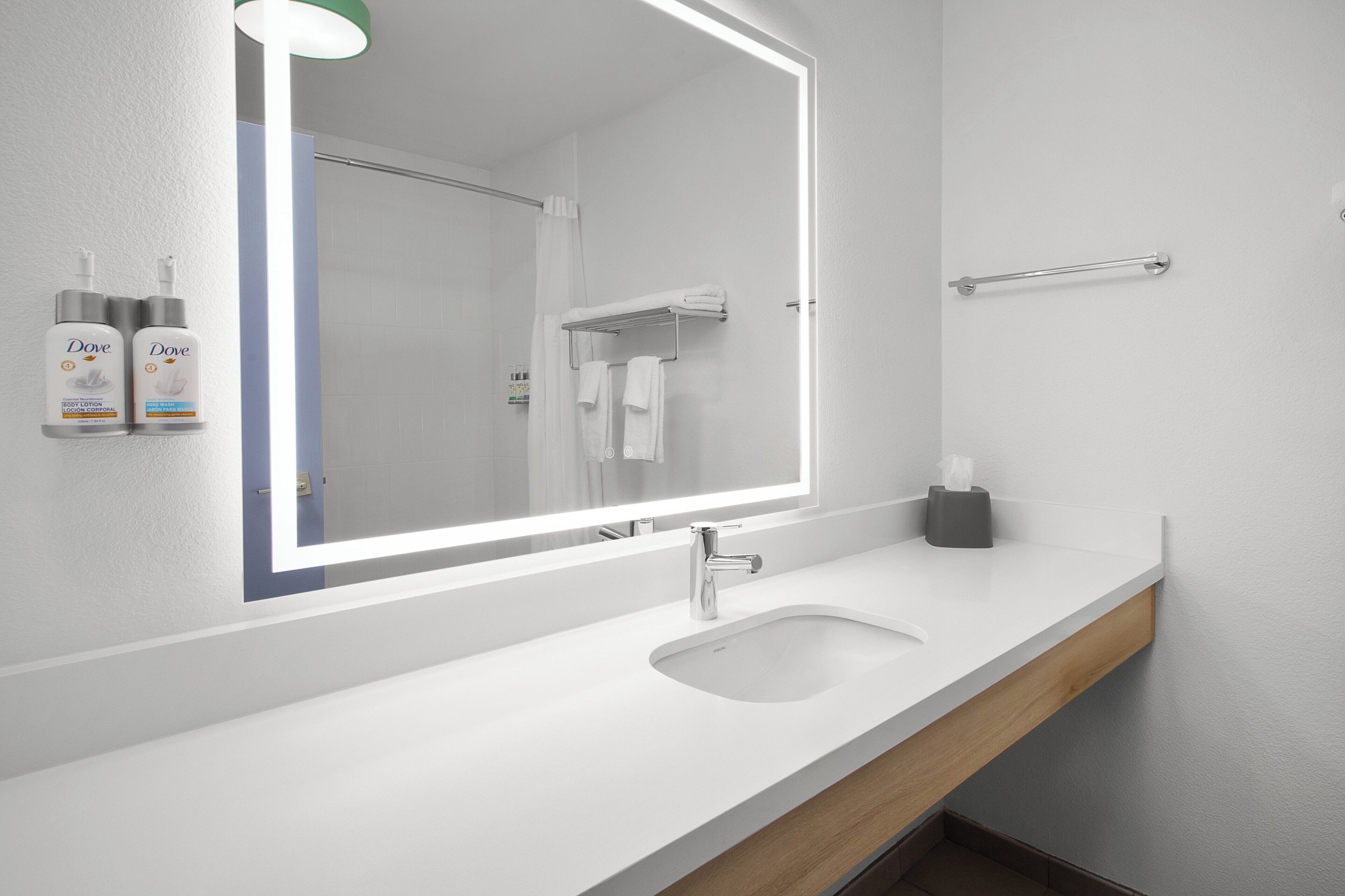 Un baño moderno con un lavabo blanco, un espejo iluminado y botellas de Dove.