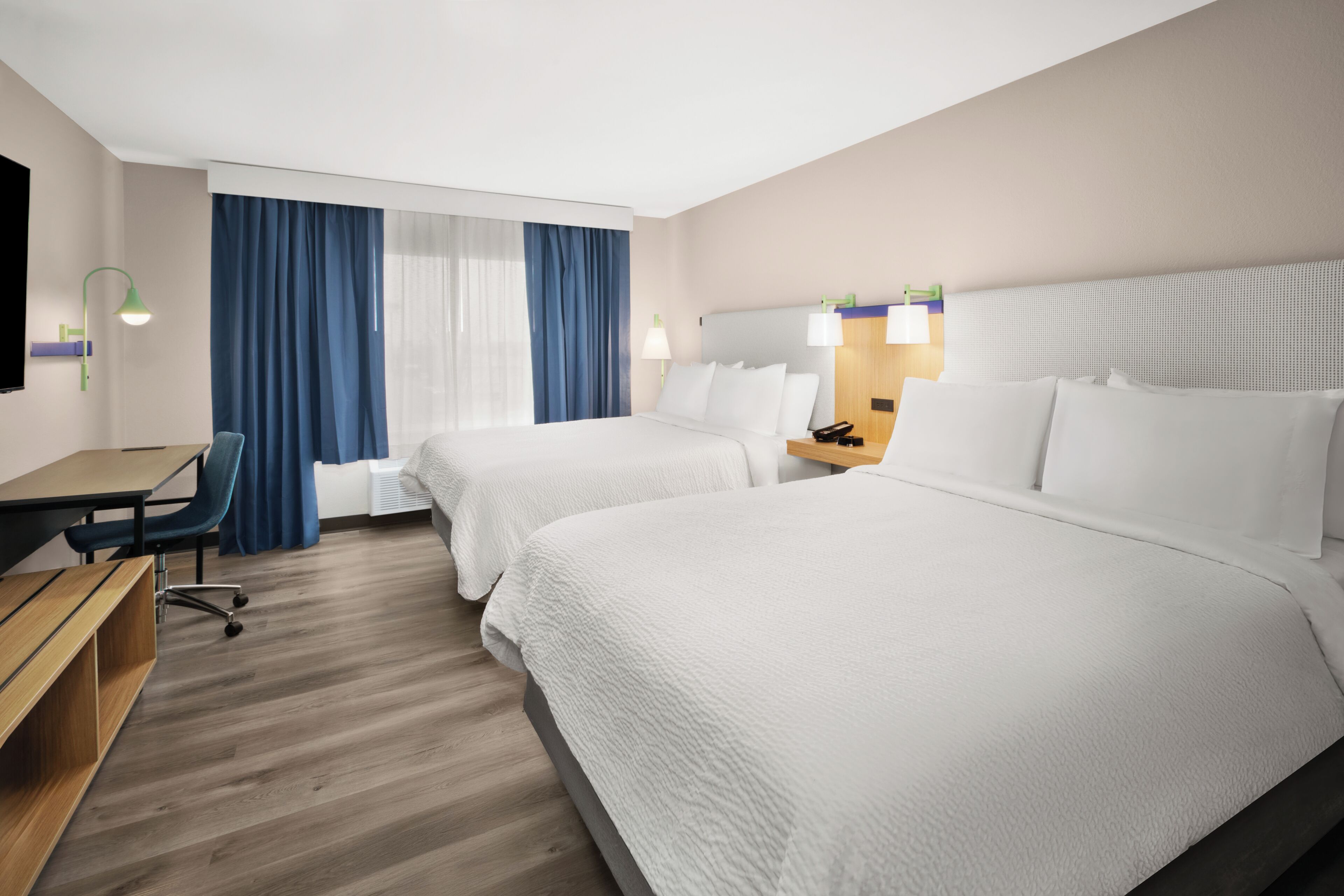 Quarto de hotel com duas camas, uma escrivaninha, uma cadeira e uma televisão.