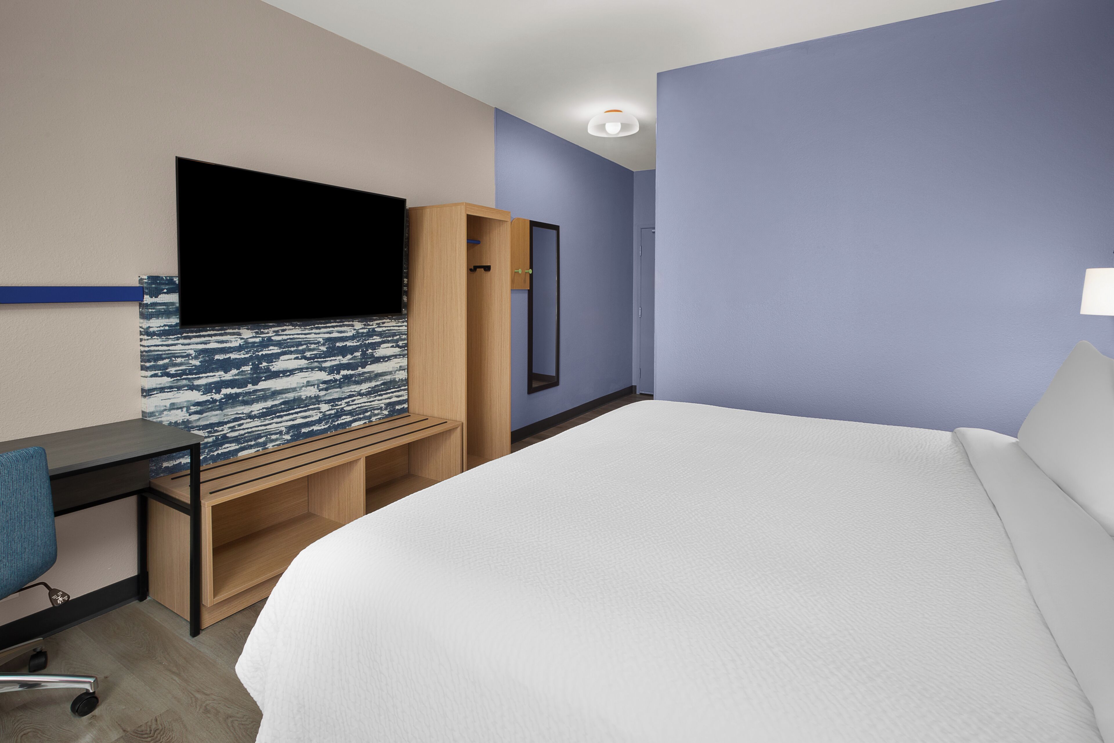 A hotel room with a bed, a desk, a chair, a TV, and a wardrobe.
