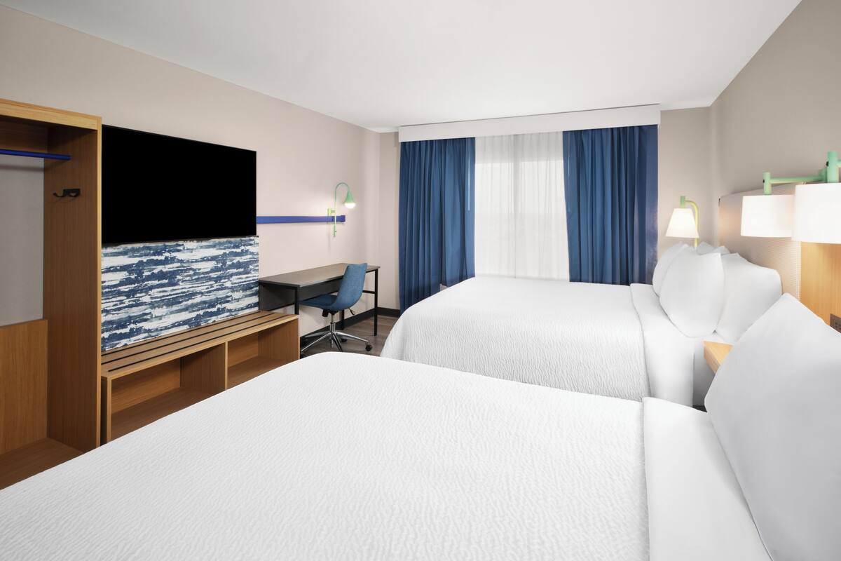 Habitación de hotel con dos camas, un escritorio, una silla, un televisor y una ventana con cortinas.