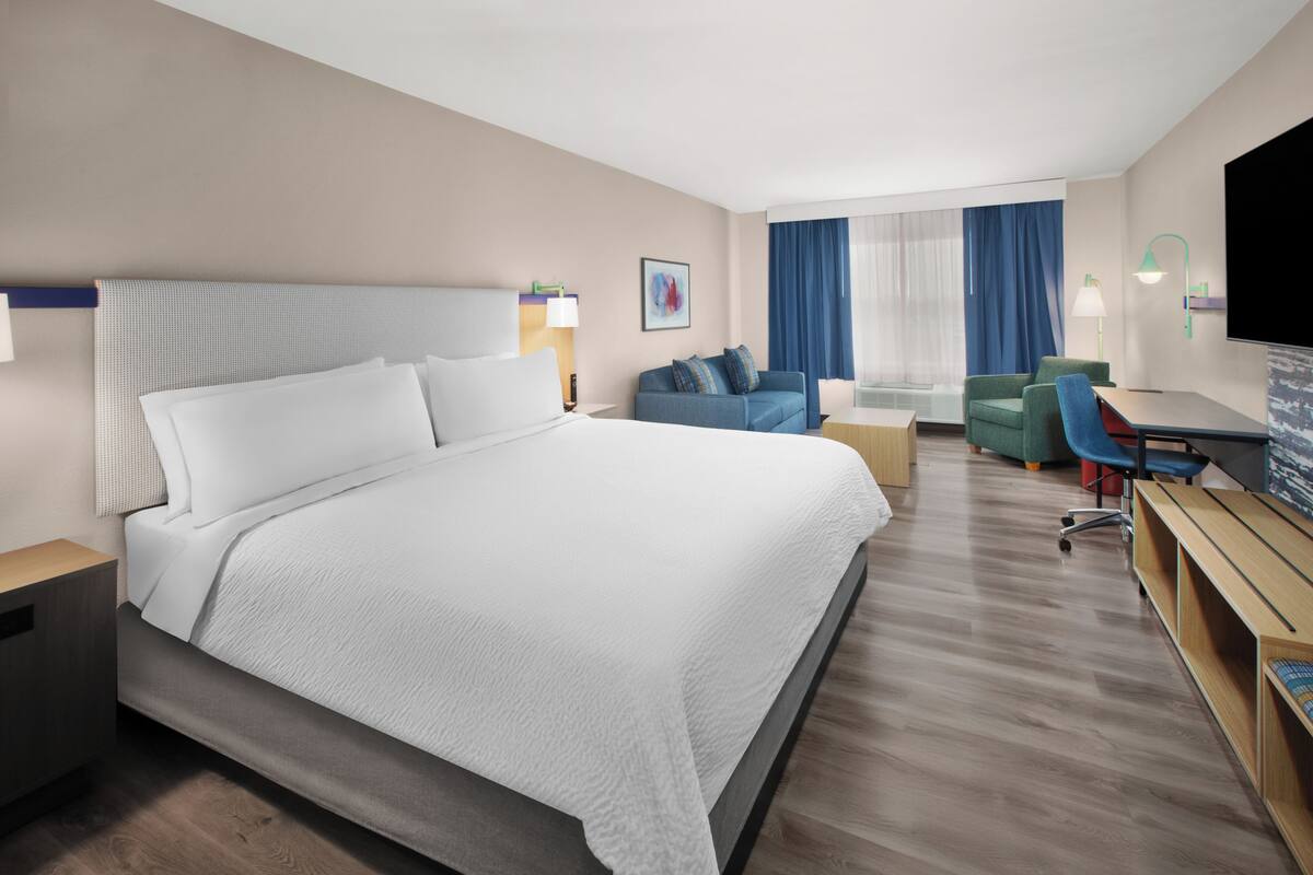Habitación de hotel con una cama grande, un escritorio, una silla, un sofá y un televisor.