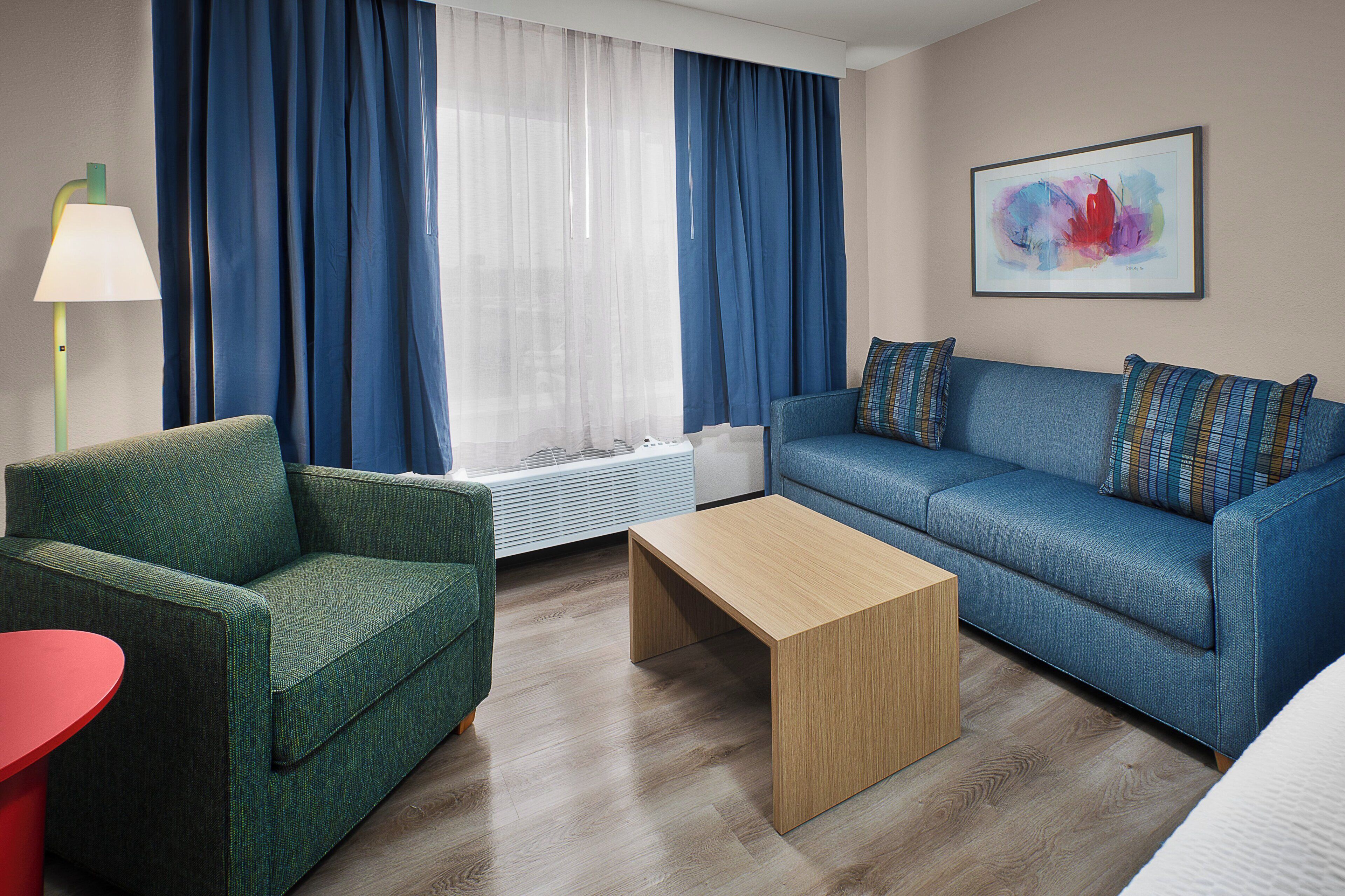 Una sala de estar moderna con un sillón verde, un sofá azul, una mesa de centro de madera y una mesita auxiliar roja.