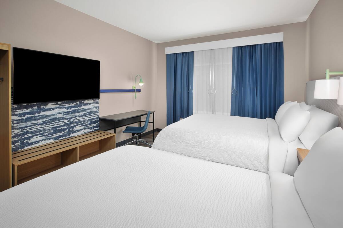 Habitación de hotel con dos camas, un escritorio, un televisor de pantalla plana y un ventanal con cortinas.