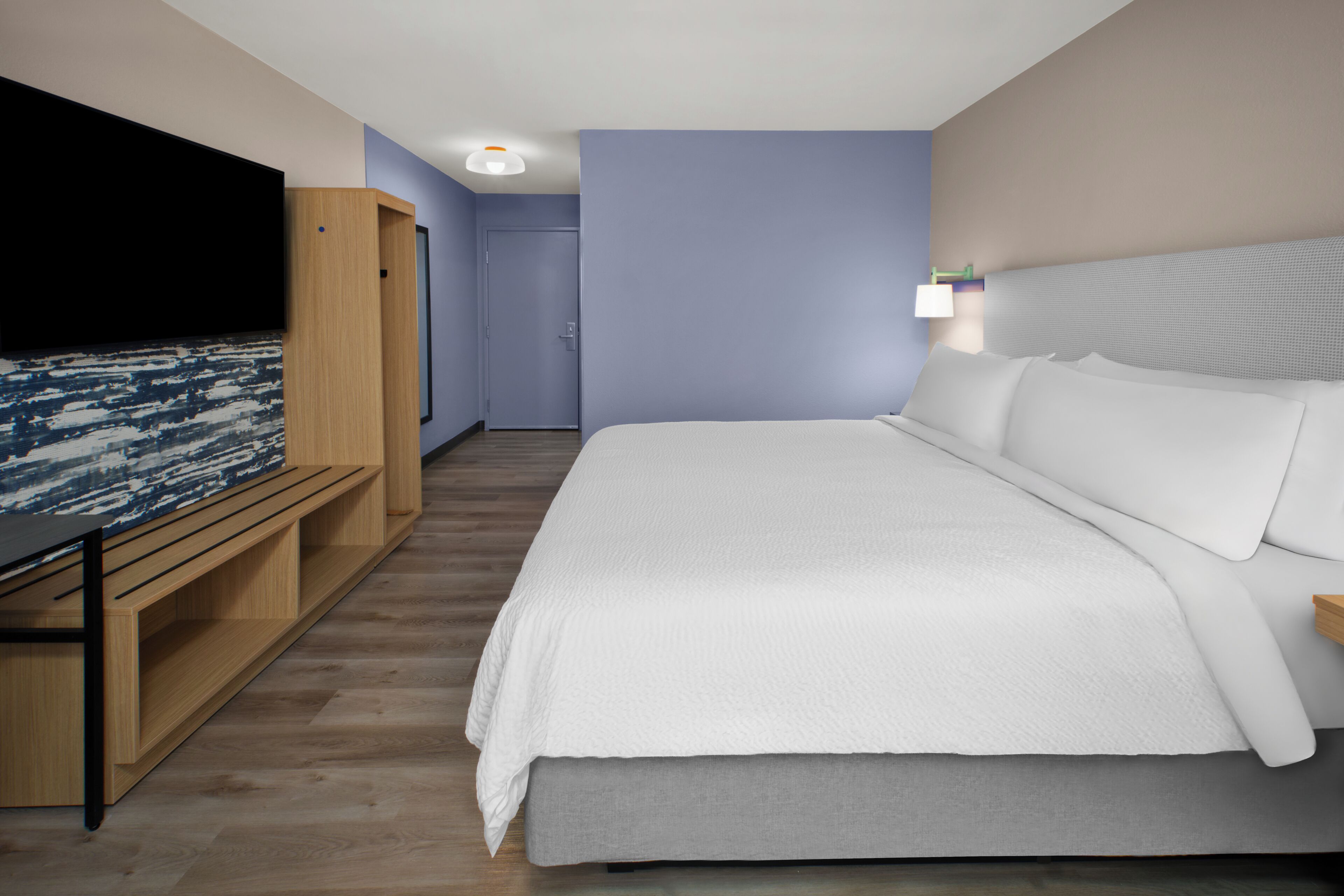 Una habitación de hotel moderna con una cama grande, un televisor, un banco de madera y una puerta que da a otra habitación.