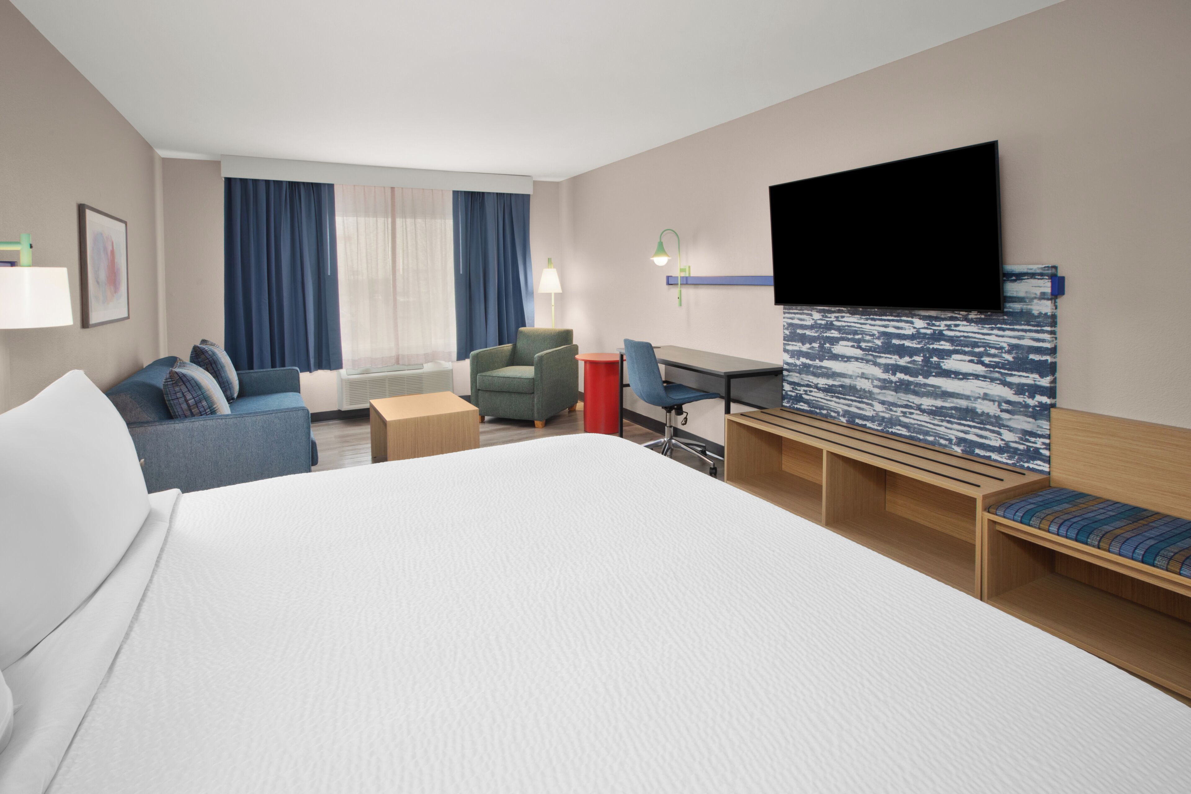 Une chambre d’hôtel avec un grand lit, un bureau, une chaise, un canapé, une télévision et une fenêtre avec des rideaux.