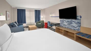 Une chambre d’hôtel avec un grand lit, un bureau, une chaise, un canapé, une télévision et une fenêtre avec des rideaux.