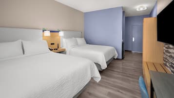 Une chambre d’hôtel avec deux lits, un bureau, une chaise, une télévision et une porte donnant sur une autre pièce.