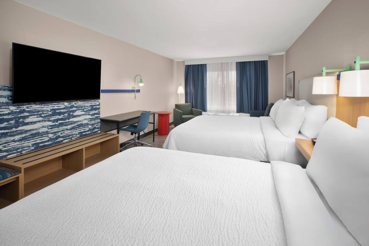 Una habitación de hotel con dos camas, un escritorio, una silla, un televisor y una ventana con cortinas.