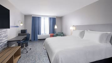 A hotel room with a large bed, a desk, a chair, a TV, and a window with curtains.