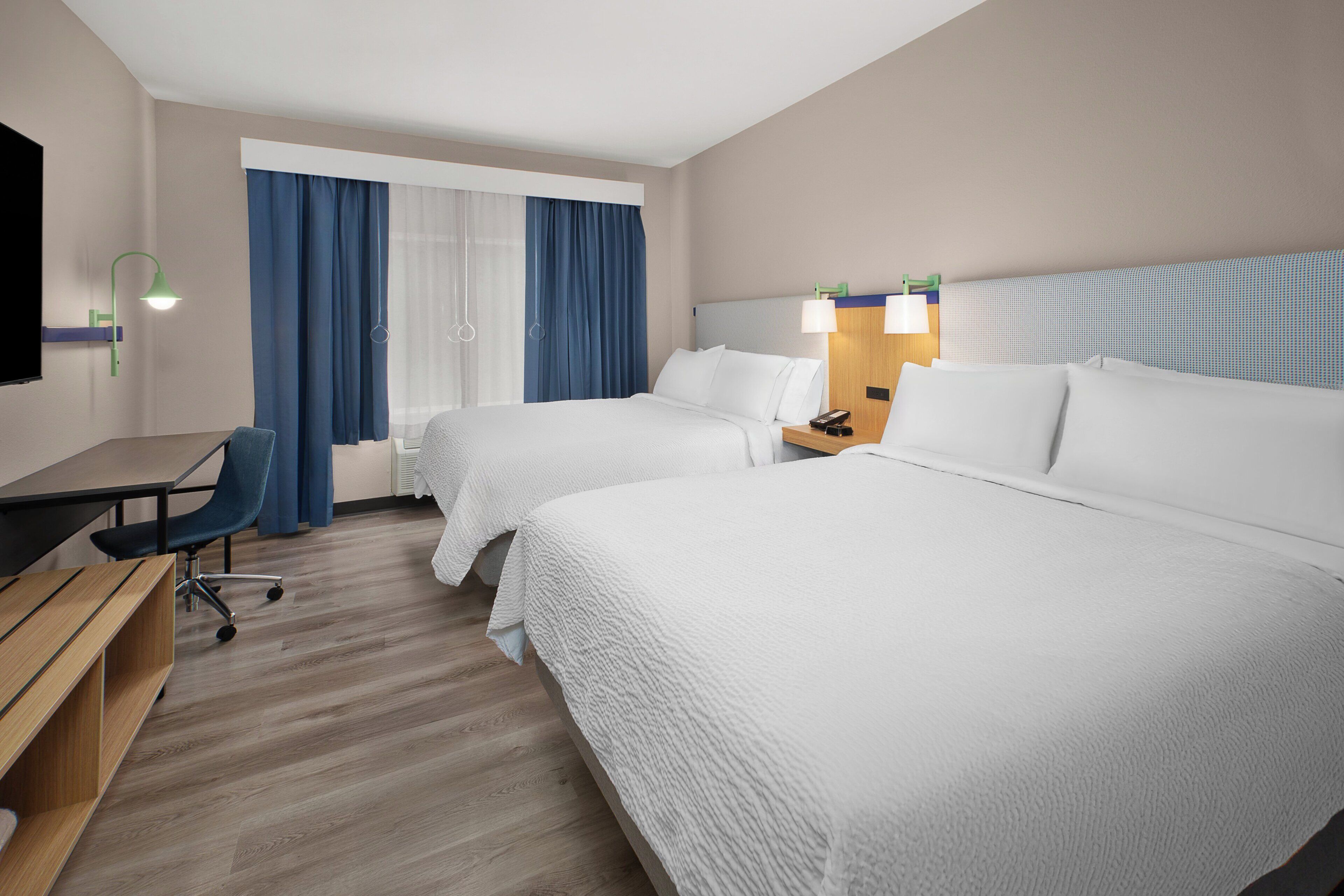 A hotel room with two beds, a desk, a chair, and a TV.