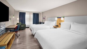 Une chambre d’hôtel avec deux lits, un bureau, une chaise, une télévision et une fenêtre avec des rideaux.
