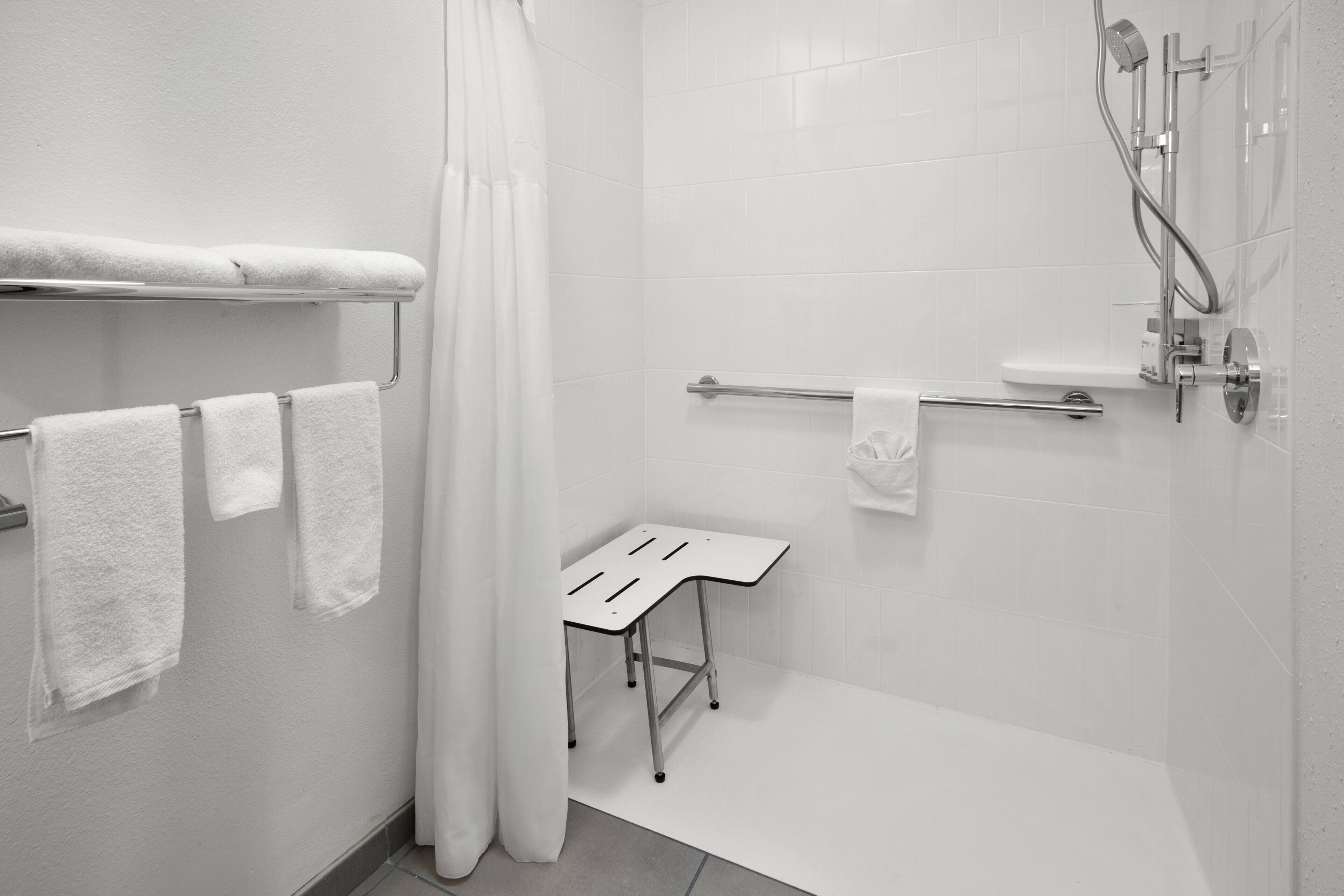 A modern bathroom with white tiles, a shower, a towel rack, and a small table.