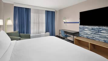 A hotel room with a large bed, a desk, a chair, a TV, and a window with curtains.