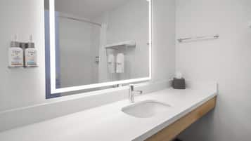 A modern bathroom with a white sink, a mirror with integrated lighting, a towel rack, and Dove lotion dispensers.
