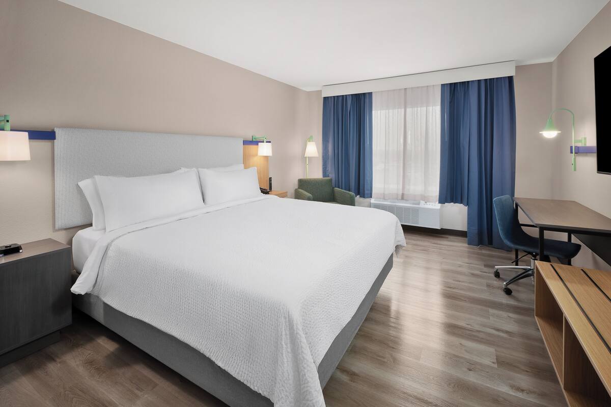 Una habitación de hotel con una cama grande, un escritorio, una silla, una mesita de noche y un televisor.