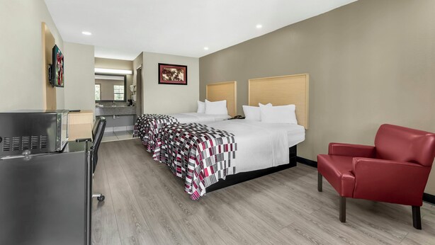 A hotel room with a bed, a red chair, a desk, and a kitchenette. - Red Roof Inn West Memphis, AR (West Memphis)