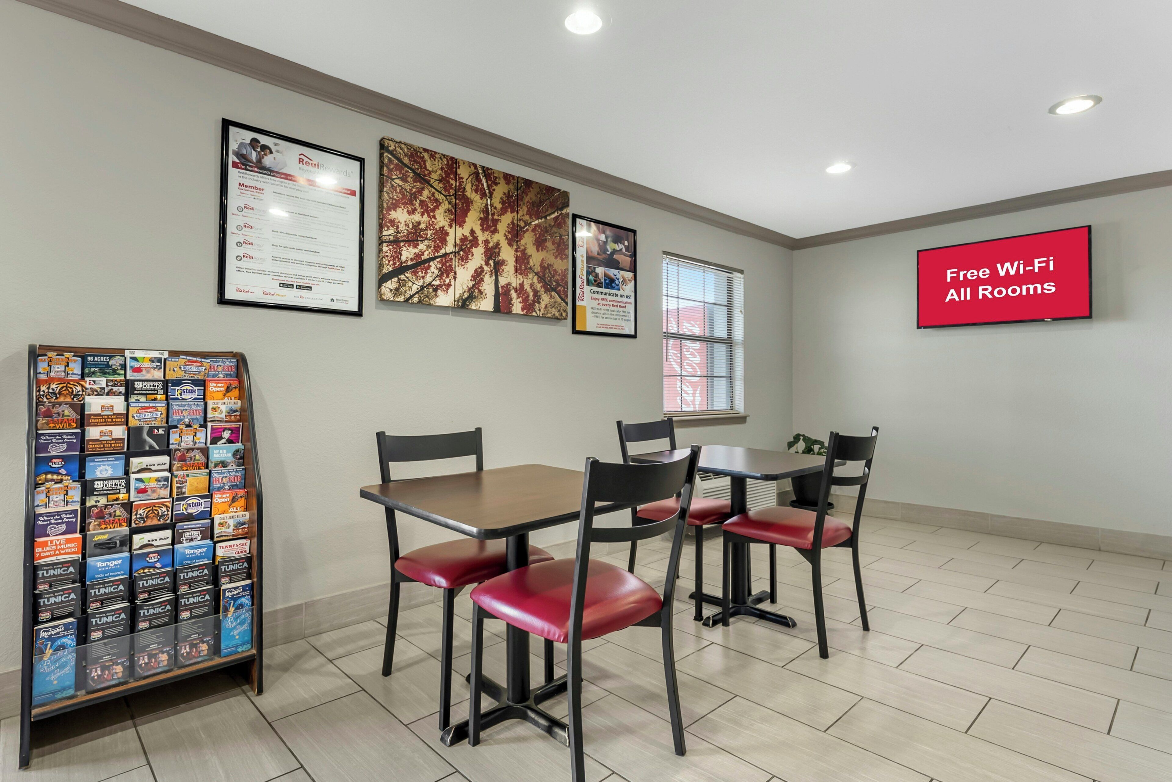 A conference room with tables and chairs, framed pictures on the walls, a bulletin board with brochures, and a sign indicating free Wi-Fi.