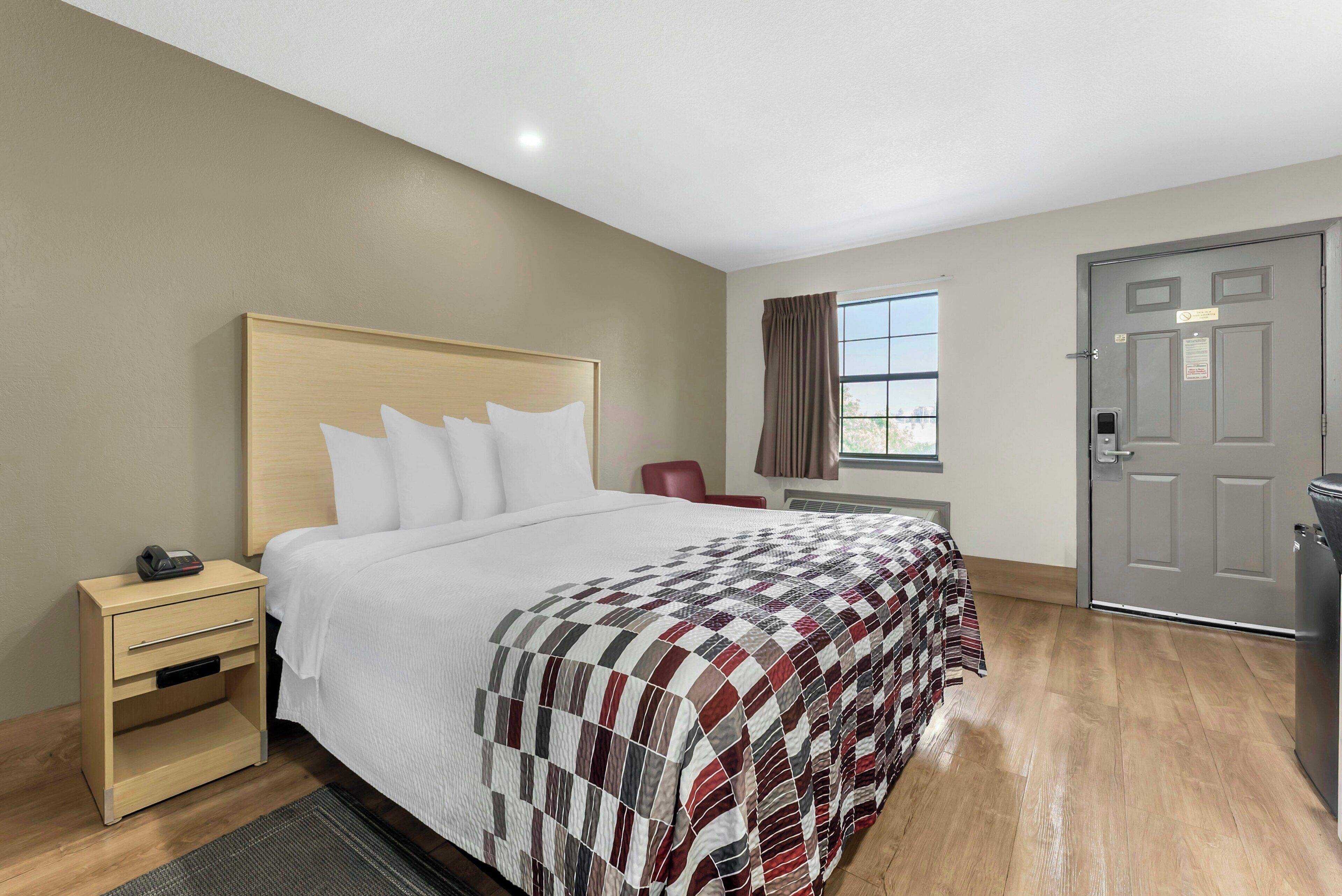 A hotel room with a bed, bedside table, chair, window, and door.