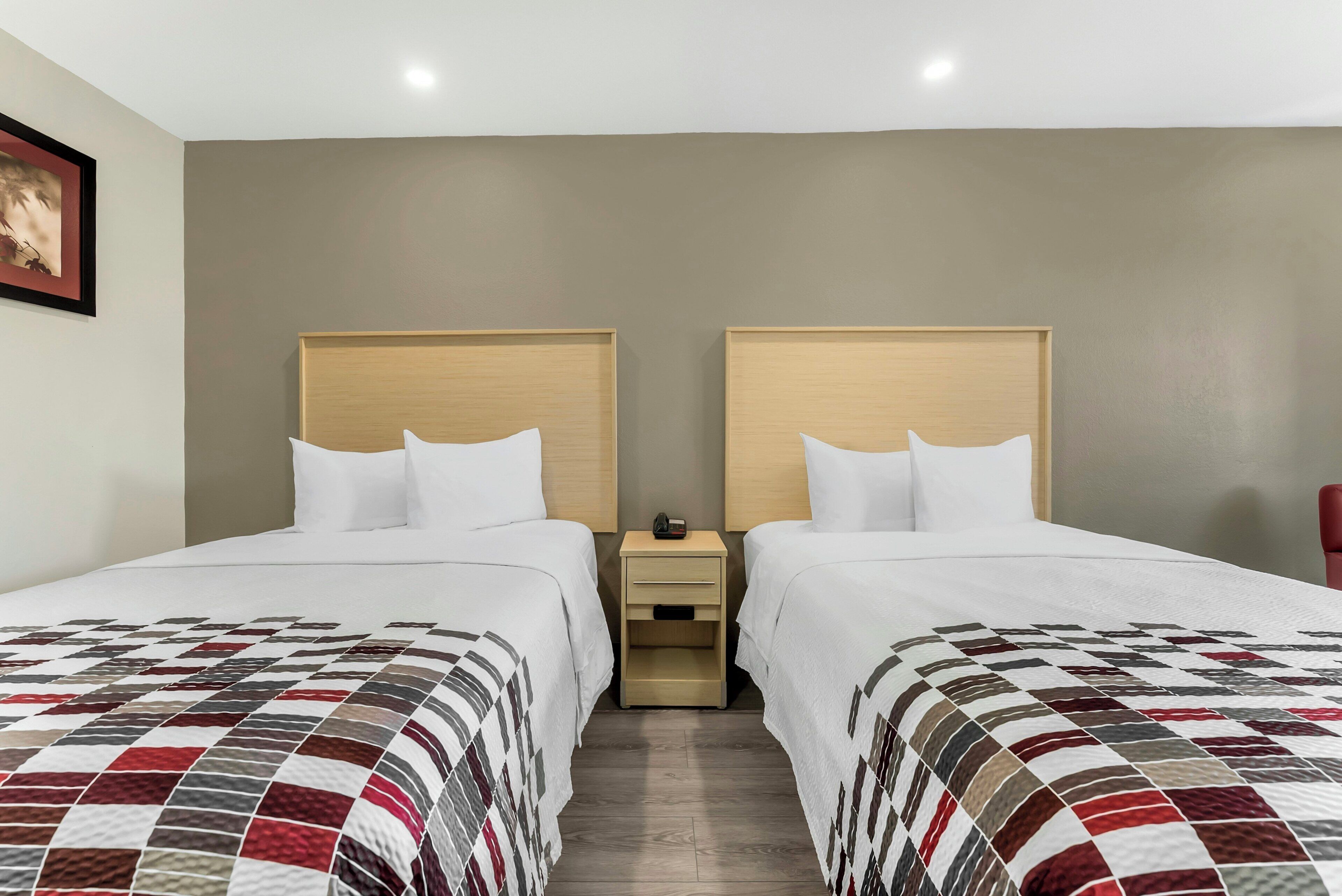 Une chambre d’hôtel avec deux lits, une table de chevet et un tableau encadré au mur.