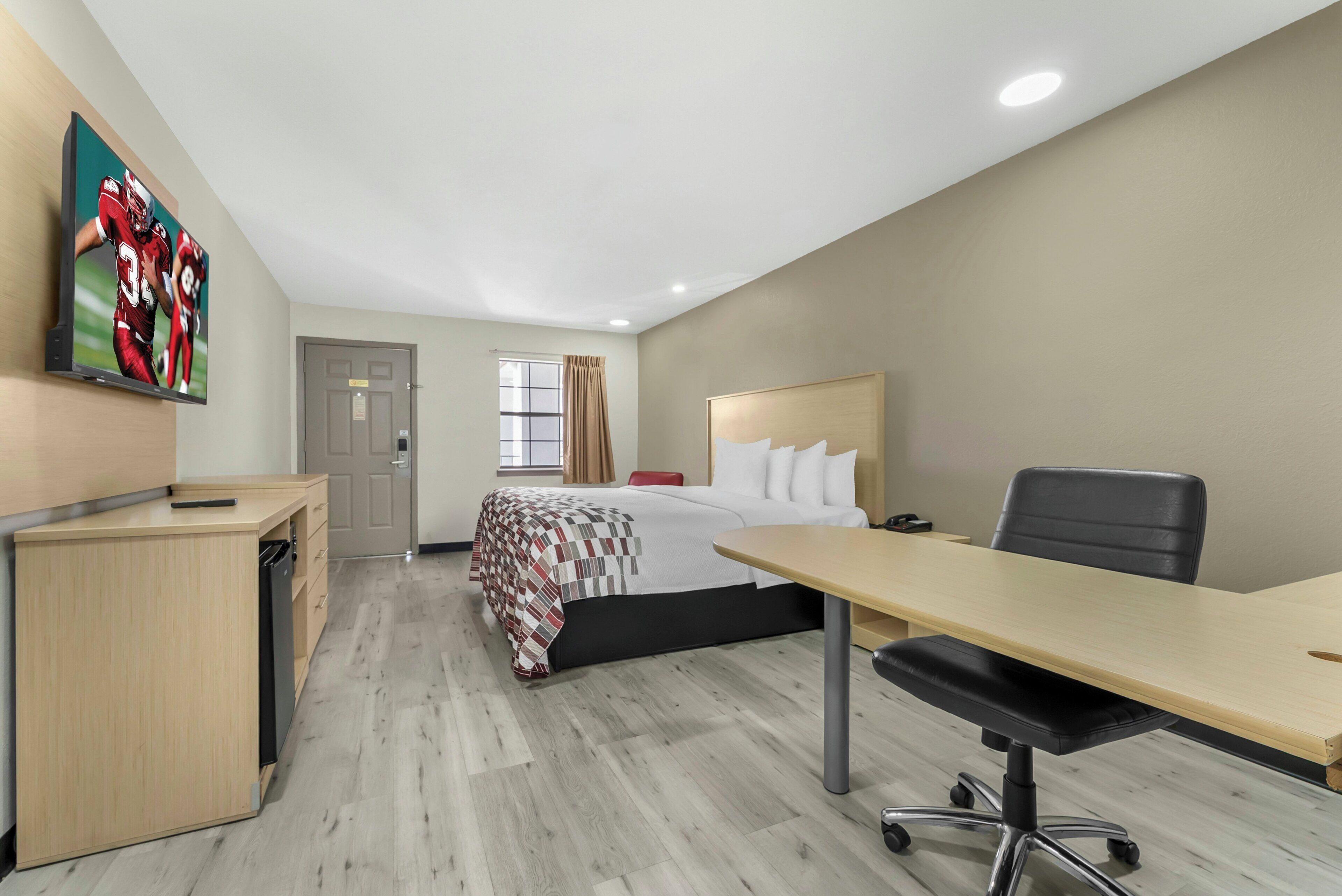 Une chambre d’hôtel avec un lit, un bureau, une chaise et un téléviseur fixé au mur.