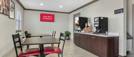 Quarto de hotel com mesa de jantar, cadeiras, área de cozinha com máquina de gelo e placa indicando Wi-Fi gratuito.