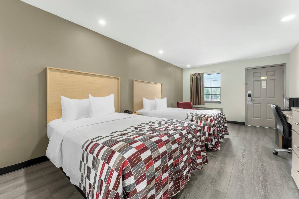 Une chambre d’hôtel avec deux lits, un bureau, une chaise et une porte.