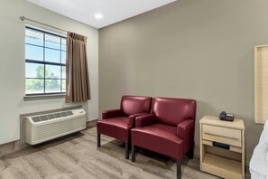 A hotel room with a window, a red leather sofa, a bedside table with a phone, and a built-in air conditioner. - Red Roof Inn West Memphis, AR (West Memphis)