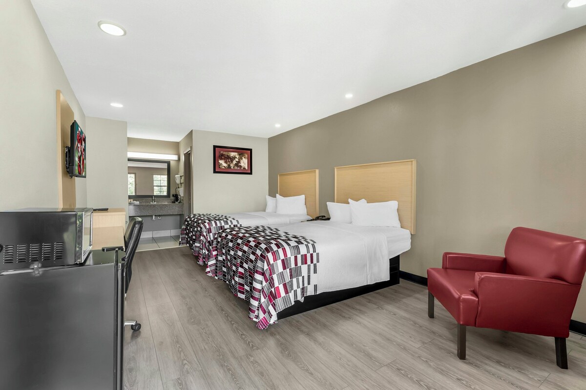 A hotel room with a bed, a red chair, a desk, and a kitchenette.
