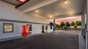 En tankstation med en Coca-Cola automat, parkeringsplads under tag og udsigt til solnedgang.