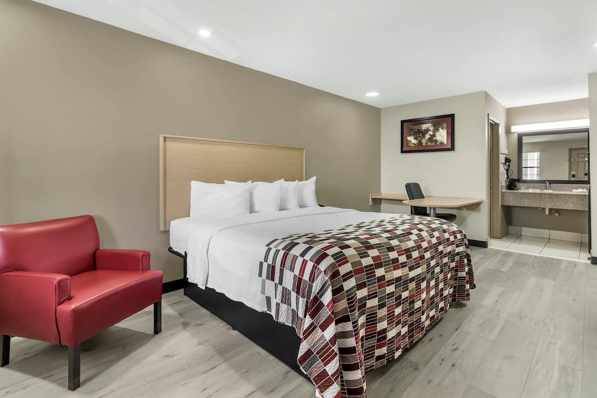 Une chambre d’hôtel avec un lit, une chaise rouge, un bureau et une salle de bain avec un miroir.