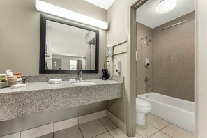 A bathroom with a granite countertop, two sinks, a large mirror, a hairdryer, a shower, and a toilet. - Red Roof Inn West Memphis, AR (West Memphis)