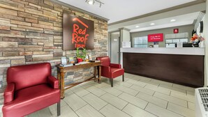 A Red Roof Inn reception area with a stone wall, a reception desk, two red chairs, and a sign indicating free Wi-Fi in all rooms. - Red Roof Inn West Memphis, AR (West Memphis)