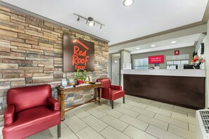 A Red Roof Inn reception area with a stone wall, a reception desk, two red chairs, and a sign indicating free Wi-Fi in all rooms. - Red Roof Inn West Memphis, AR (West Memphis)