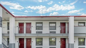 A multi-story building with red doors, windows, and a balcony. - Red Roof Inn West Memphis, AR (West Memphis)