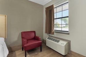A room with a red chair, a window with curtains, a radiator, and a wooden floor. - Red Roof Inn West Memphis, AR (West Memphis)