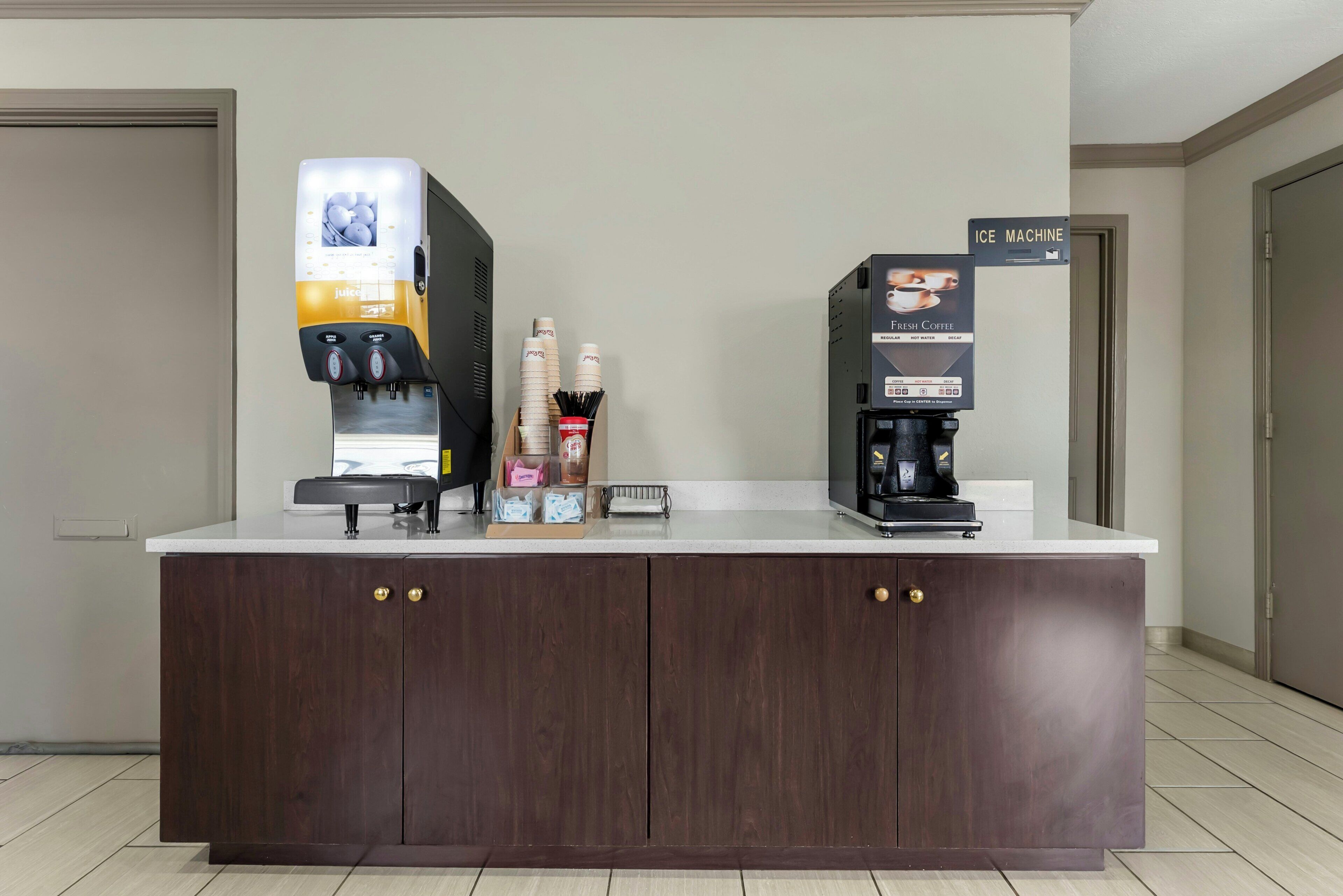 Mostrador con una máquina de café, dispensador de jugo y señalización para una máquina de hielo.