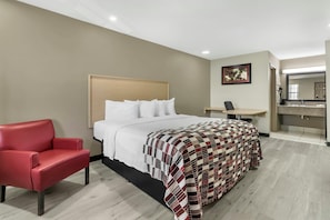 A hotel room with a bed, a red chair, a desk, and a bathroom with a mirror. - Red Roof Inn West Memphis, AR (West Memphis)