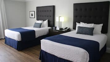 Habitación de hotel con dos camas, cada una con cabecero oscuro y ropa de cama blanca. Entre las camas, una mesita de noche con lámpara y teléfono.