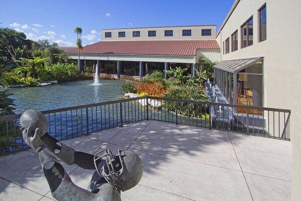 A courtyard with a fountain, a statue, and a building with a red roof. - Miami Lakes Hotel (Miami Lakes)