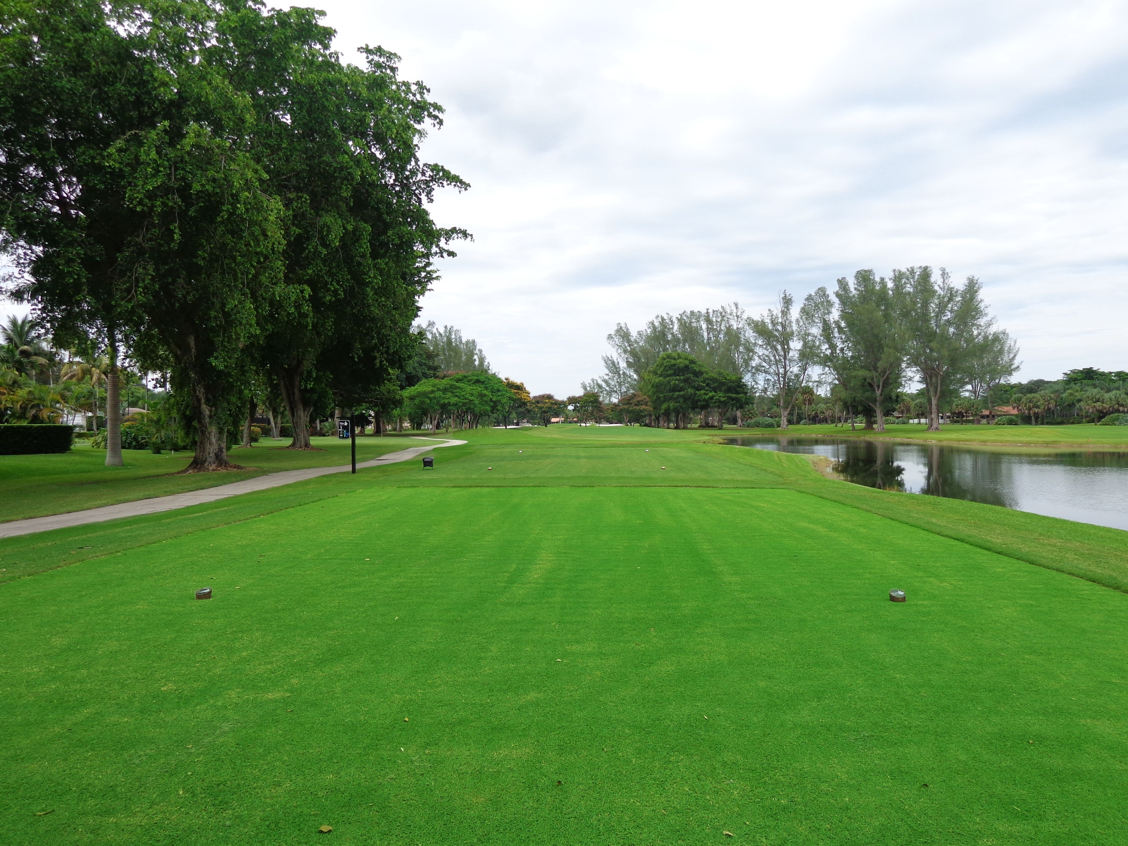 Un campo de golf bien cuidado con un estanque, árboles y un sendero para caminar.