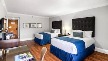 Habitación de hotel con dos camas, un escritorio y una silla. Hay cuadros en la pared y una lámpara en la mesita de noche.