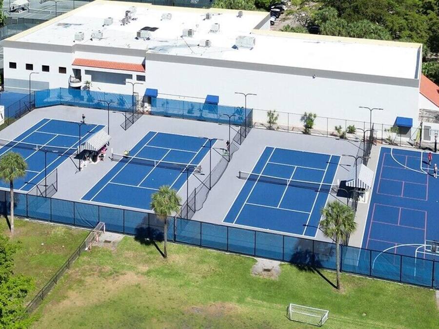 An aerial view of a sports complex with multiple tennis courts, a basketball court, and a building with a red roof.