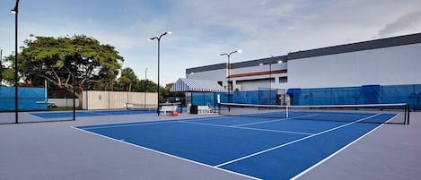En utomhusbana för tennis med nät, omgiven av staket och gatlyktor.